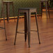 A close-up of a Lancaster Table & Seating backless copper bar stool with a black wood seat.
