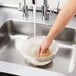 A hand washing rice and grains in an OXO plastic colander on a counter.