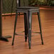 A Lancaster Table & Seating black metal counter height stool with a black wood seat on a wood floor.