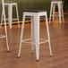 A set of three Lancaster Table & Seating white metal backless bar stools with black wood seats.