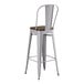 A white metal Lancaster Table & Seating barstool with a walnut wood seat.