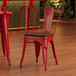 A red Lancaster Table & Seating cafe chair with black wood seat at a table in a restaurant.