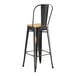 A black metal Lancaster Table & Seating barstool with natural wood seat.