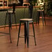 A Lancaster Table & Seating black metal cafe barstool with a natural wood seat.