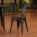 A Lancaster Table & Seating black metal chair with a walnut wood seat at a table in a restaurant.