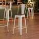 A white Lancaster Table & Seating barstool with a walnut wood seat.