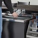 A person holding a clear glass while another person fills it with a clear bottle of alcohol on a counter.