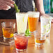 A bartender pouring drinks into Acopa Select stackable cooler/mixing glasses on a bar table.