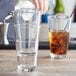 A man pouring brown liquid from a bottle into an Acopa Select stackable cooler/mixing glass.