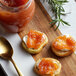 A jar of Dalmatia Quince Spread on a table with a spoon, bread, and food.