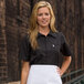 A woman wearing a black Uncommon Chef cook shirt with a full mesh back and white apron.