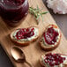 A wooden cutting board with a jar of Dalmatia Sour Cherry Spread and slices of bread with jam.