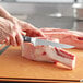 A person using a Wusthof Classic Ikon boning knife to cut meat on a cutting board.