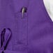 A purple Uncommon Chef bib apron with a pen in the pocket on a counter.