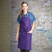 A woman wearing a purple Uncommon Chef bib apron with three pockets.