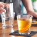 A hand pouring a drink into an Acopa Select Stackable Rocks glass on a table.