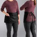 A black waist apron with three pockets, shown tied around the waist of a person.