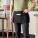A black waist apron with three pockets, worn by a person and designed for use in hospitality settings.