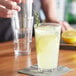 A person pouring a glass of lemonade with ice and lemon slices using an Acopa Select stackable beverage glass.