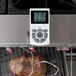 A white CDN digital thermometer with a cord checking the temperature of meat on a grill.