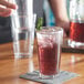 A person holding an Acopa Select highball glass filled with red liquid and ice on a napkin.