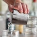 A person using an American Metalcraft stainless steel short cocktail shaker to pour liquid into a glass on a counter.