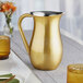 An American Metalcraft gold satin finish stainless steel bell pitcher on a table.