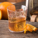 A Carlisle plastic rocks glass filled with liquid, ice, and a slice of orange.