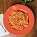 A plate of spaghetti with sauce on it and a bowl of salad on a table with a fork.