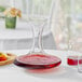 A Stolzle glass decanter filled with red liquid on a table next to glasses and a plate of fruit.