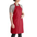 A woman wearing a burgundy Intedge bib apron with 2 pockets.