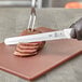 A person using a Mercer Culinary Ultimate White serrated edge slicer knife to cut meat.