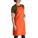 An orange Intedge bib apron with pockets on a counter.