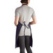 A woman wearing a navy blue Intedge bib apron with 2 pockets standing in a professional kitchen.