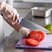 A person using a Dexter-Russell chef knife with a purple handle to slice a tomato.
