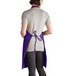 A woman wearing a purple Intedge bib apron with 2 pockets.