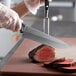 The black handle of a Dexter-Russell 8" Chef Knife cutting a piece of meat.