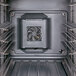 The interior of a black Cambro hot and cold food holding cabinet with metal shelves and a fan.