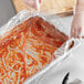 A person in gloves holding a plastic bag over a Full Size Shallow Steam Table Pan of red sauce.