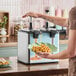 A twin topping warmer with heated spouts being used to dispense caramel sauce onto waffles.