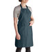 A woman wearing a hunter green Intedge poly-cotton bib apron with pockets.