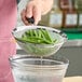 A person using an OXO Good Grips stainless steel fine mesh strainer with a black handle to strain green beans.
