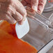 A person using a white nylon pan scraper to clean a glass container.