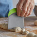 A person using a Fox Run gray plastic dough cutter with a green silicone handle to cut dough.