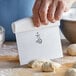 A person using a white-handled Mercer Culinary dough cutter to cut dough on a wooden table.