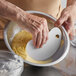 A person using a Fox Run white plastic bowl scraper to mix batter in a bowl.