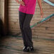 A woman wearing Uncommon Chef black pants and a pink shirt on a counter in a professional kitchen.