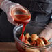 A person pouring TABASCO® Scorpion Hot Sauce onto a bowl of chicken wings.