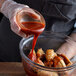 A person pouring TABASCO® Scorpion Hot Sauce onto a bowl of chicken wings.