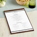 An American Metalcraft espresso wood menu holder with a rubberband holding a menu on a wood table.
